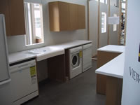 The purpose of the photograph is to show how to the Milwaukee Idea Home will construct the kitchen more accessibly. A sink, countertops, above counter cabinets, dishwasher, and clothes washer/dryer are featured in the photograph. The picture demonstrates the accessibility of the kitchen set-up with a large open space beneath the sink for easy access by a wheelchair and the washer and dryer side-by-side on the floor for easy access while seated.