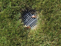 The photograph shows that a lawn drain has been installed in the ground outside, to drain rain water into the sewer system below. The drain will prevent the lawn from becoming flooded and has been constructed somewhere in the yard of the model home. The viewers are able to see that the model home includes this feature.