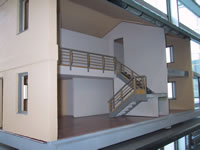 This photograph shows a stairway from the first floor of a model house display to the second floor. The stairway zigzags along the side of the wall and contains a landing halfway up. There is no furniture, windows, or doors in the photograph because the photo is mainly showing the interior layout of the house.